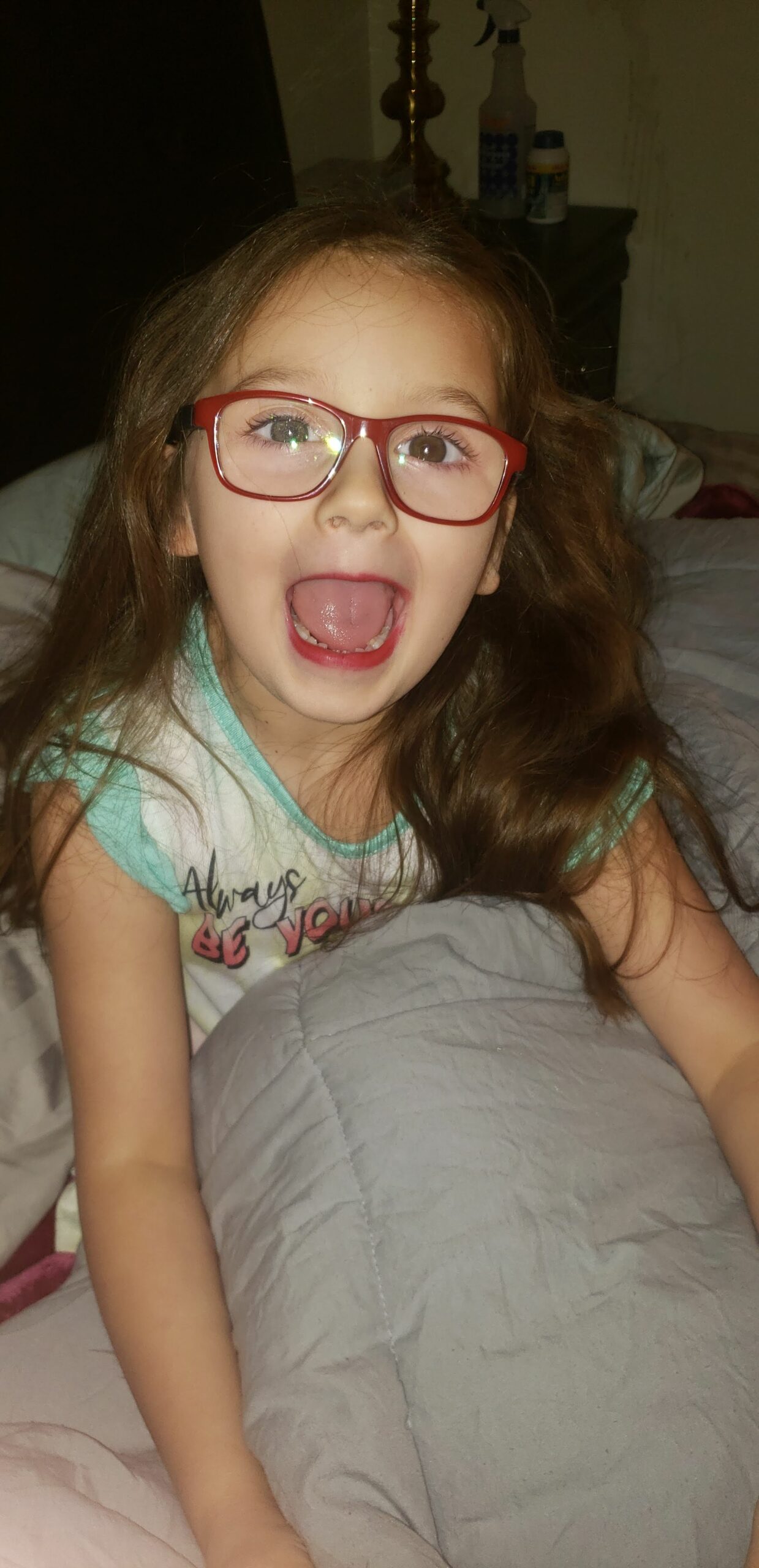 a young girl wearing glasses with very excited face laying in bed.