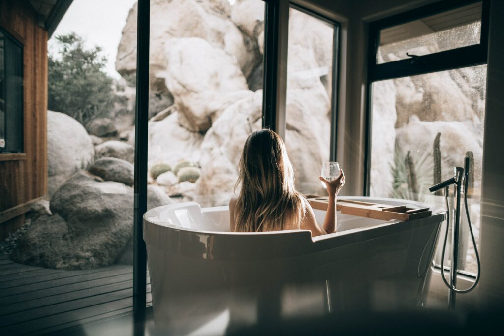 an image of a lady in a bathtub with a drink in her hand looking at the window